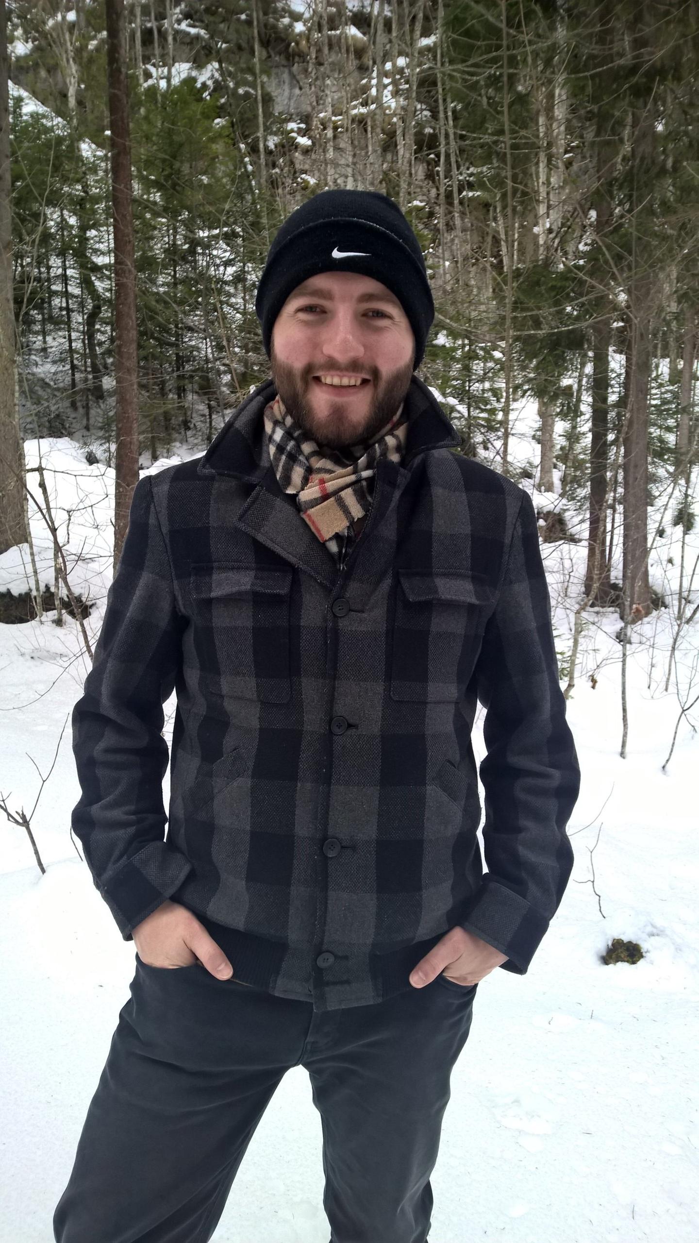 Mann mit Jacke, Halstuch und Bart in einem Wald