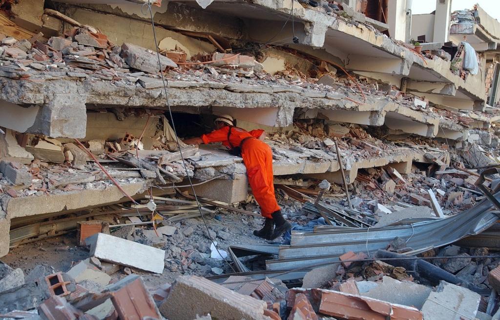 Sauveteur en tenue orange au milieu de décombres.