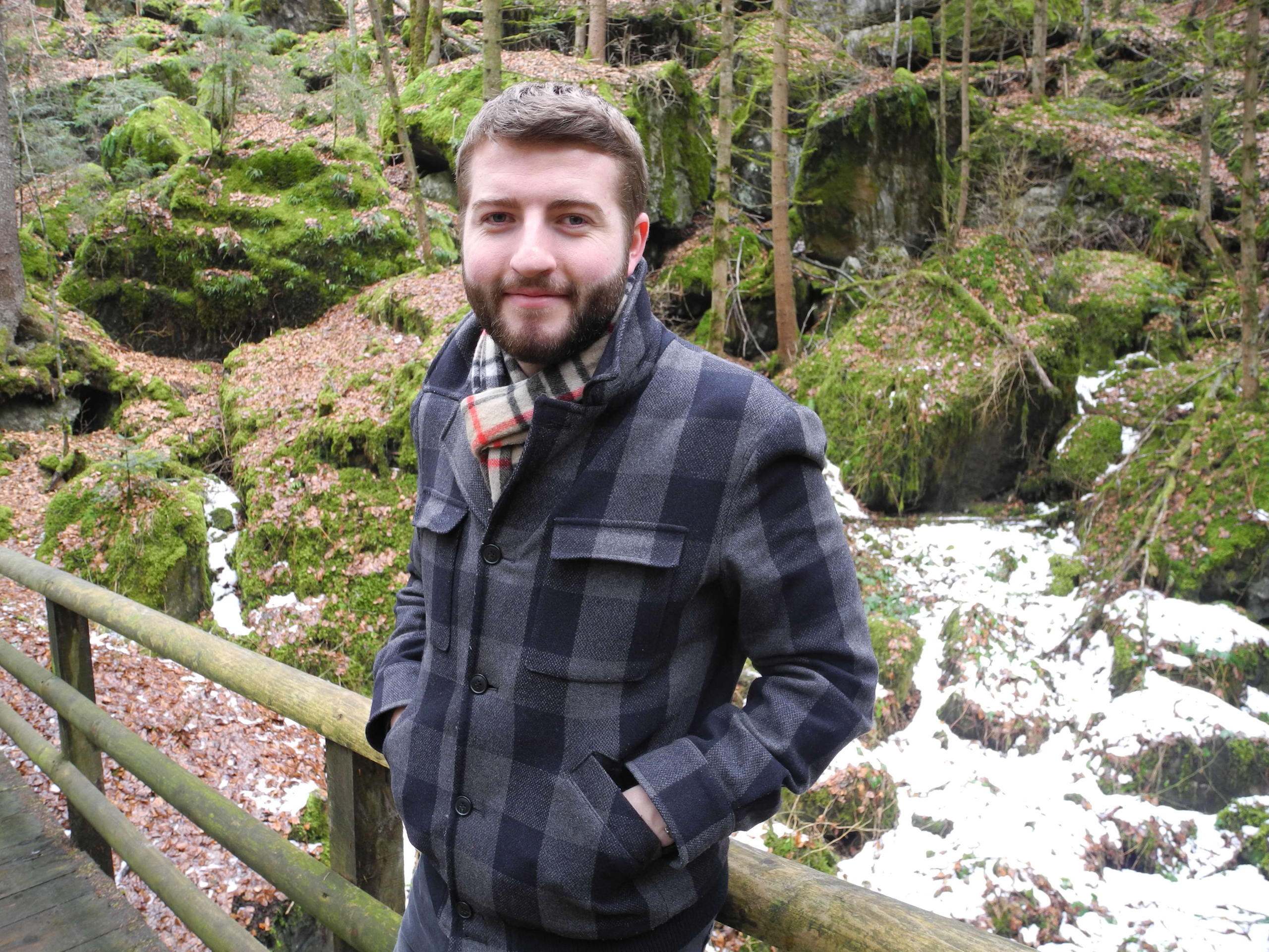 Bärtiger Mann mit Jacke und Halstuch in einem Wald