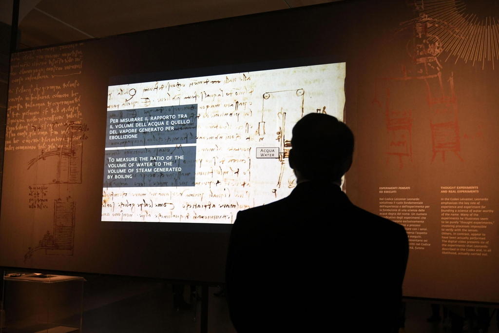 Silhouette di un uomo di schiena di fronte a un installazione multimediale che mette in luce un manoscritto