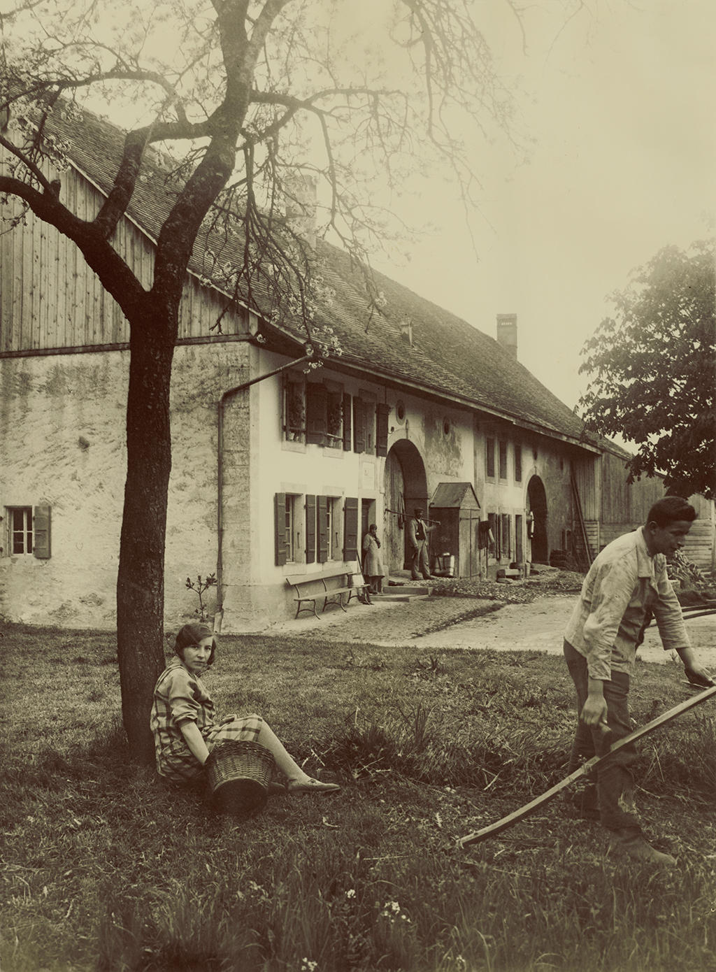 Farmhouse with people in the foreground, woman looking at the camera