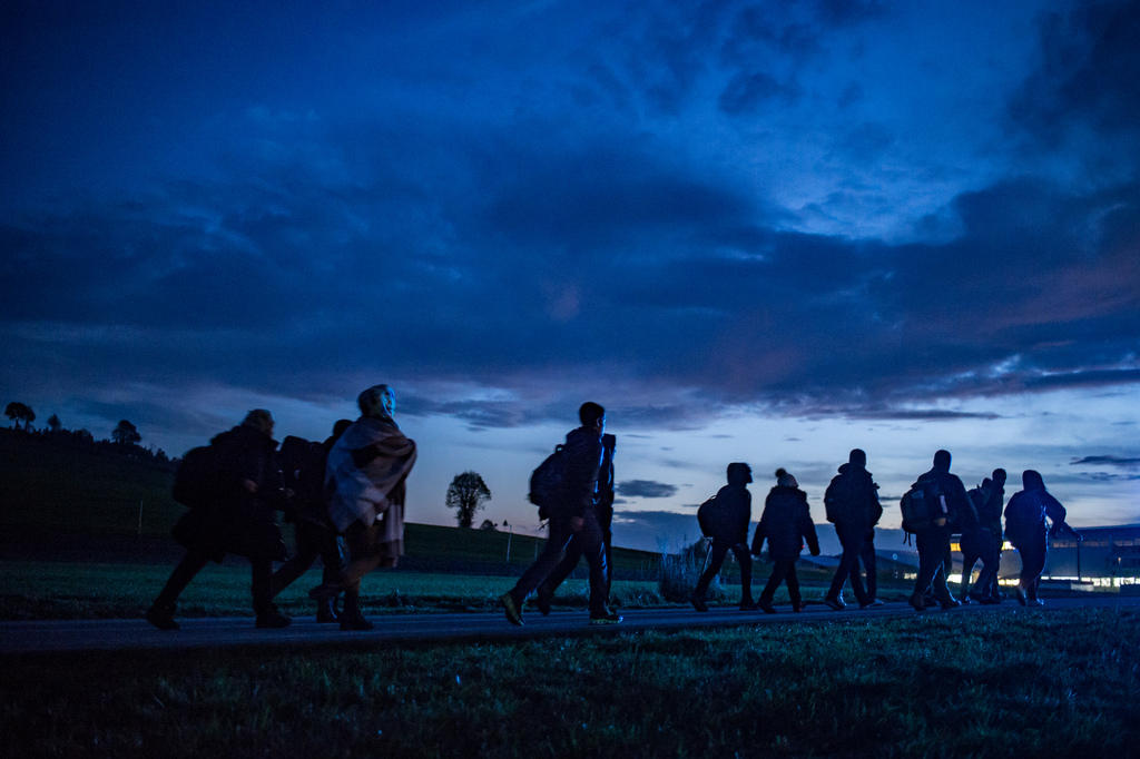 Refugees walking in border region below dark sky