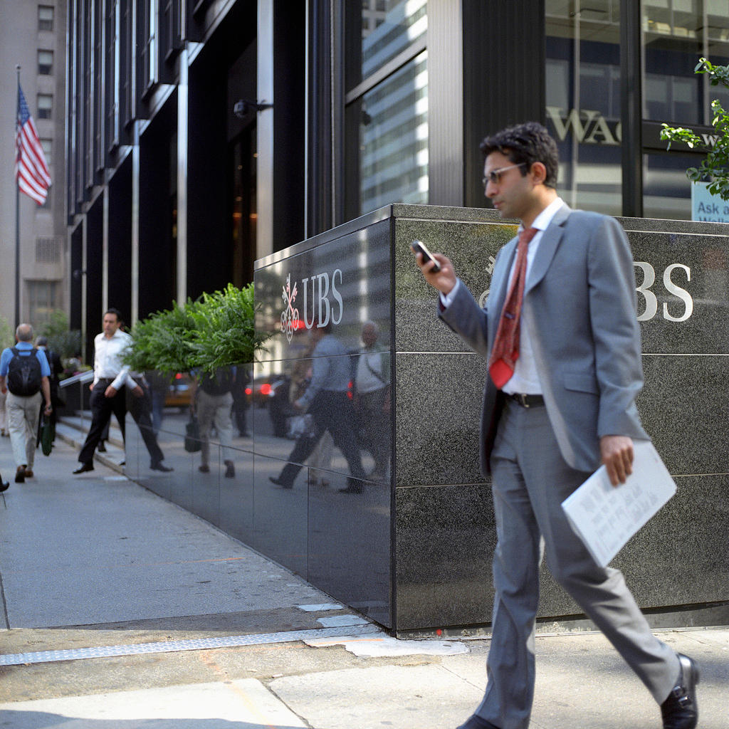 Ein Mann mit Handy steht auf dem Gehsteig vor einer UBS-Filiale in den USA.