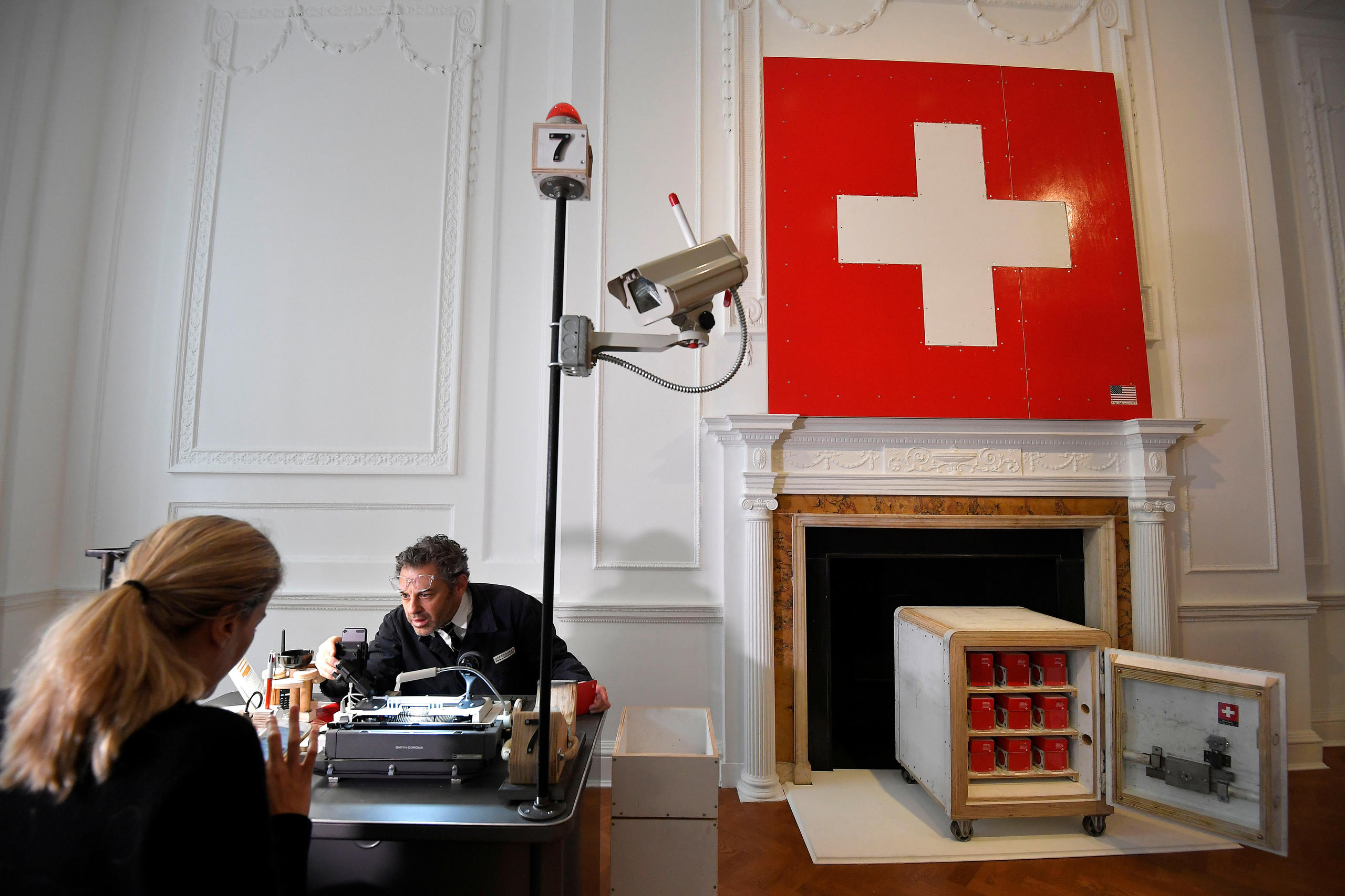 man questioning woman next to Swiss flag