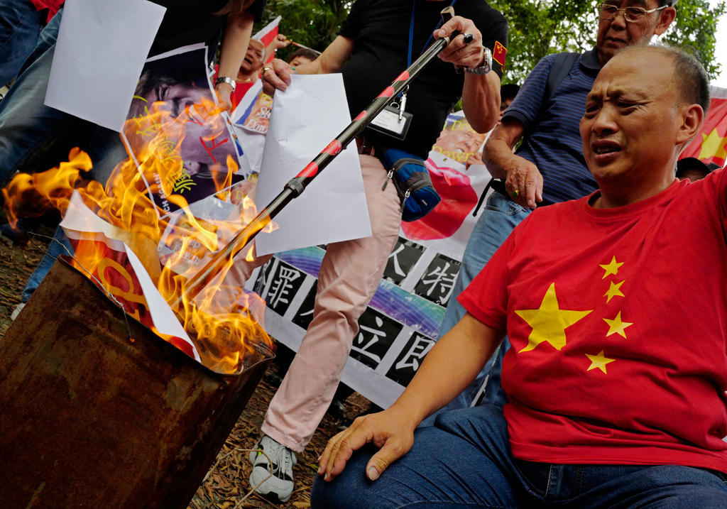 Homem com camisa da bandeira da China queima pôsteres