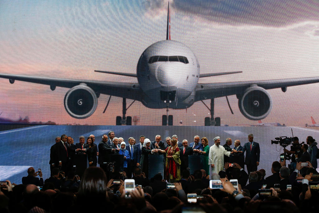 Erdogan, attorniato da invitati alla cerimonia, nella hall dell aeroporto con alle spalle l immagine gigante di un aereo