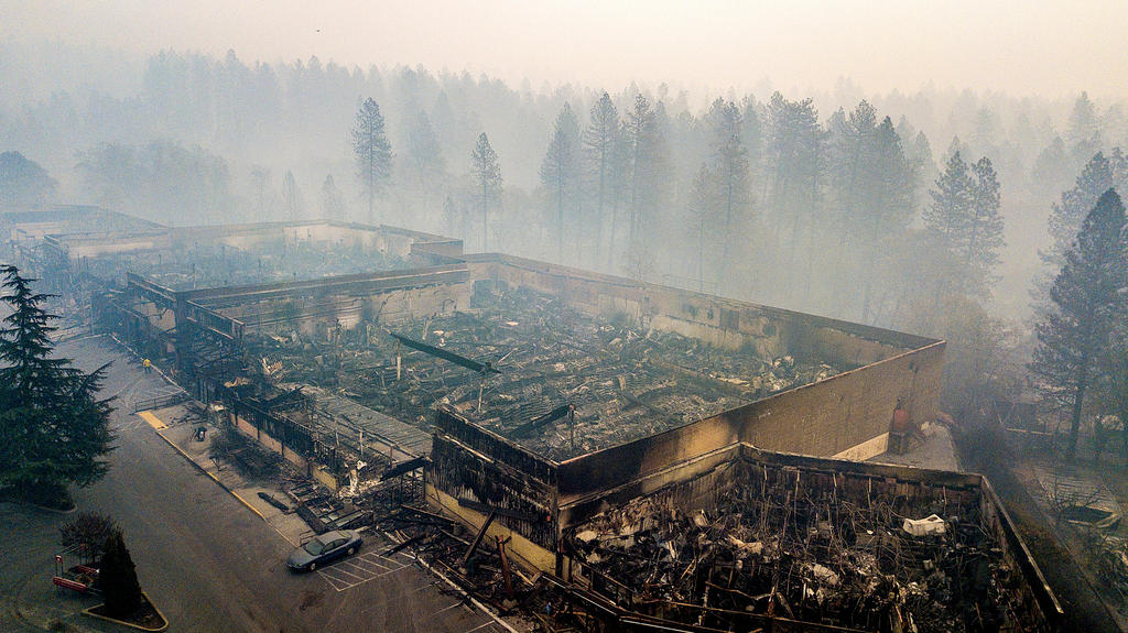Pareti esterne di un edificio visibilmente distrutto da un incendio, accanto a una foresta; fumo tutt intorno