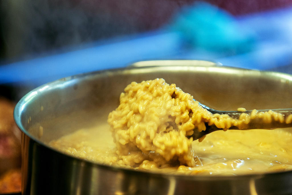 Primo piano di una pentola colma di risotto giallo e di un mestolo, che è appena stato intinto