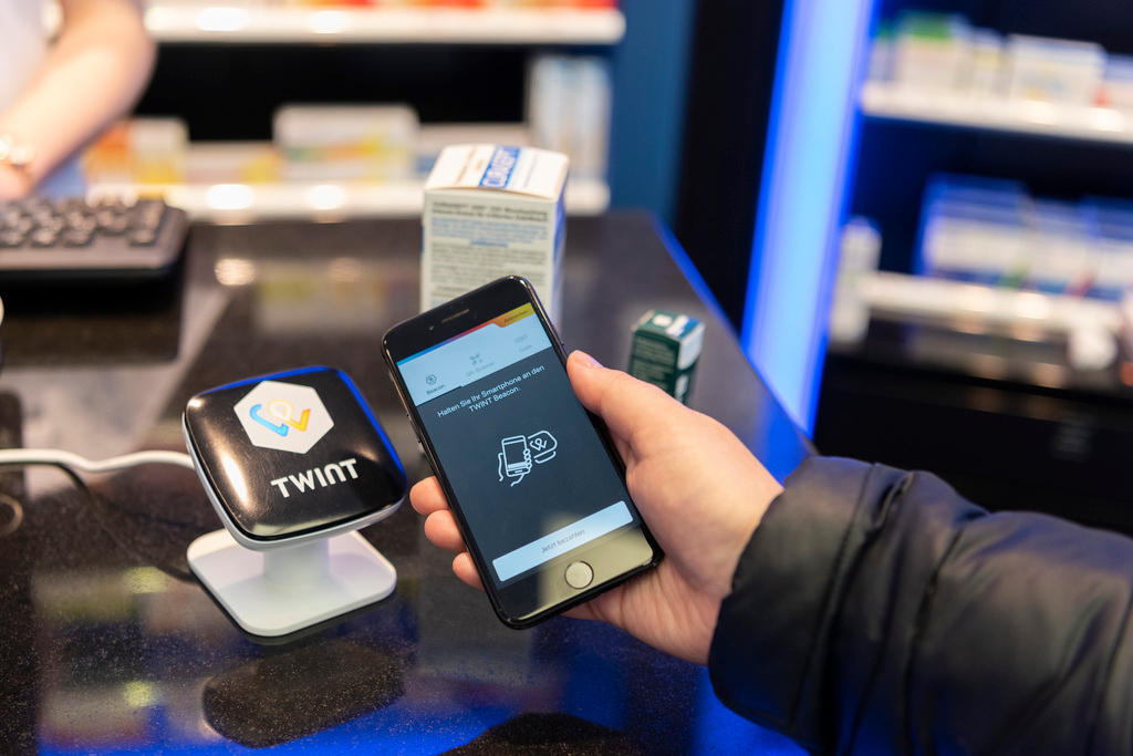 Primo piano dell avambraccio d un uomo che avvicina il suo cellulare al terminale TWINT in quella che sembra essere una farmacia