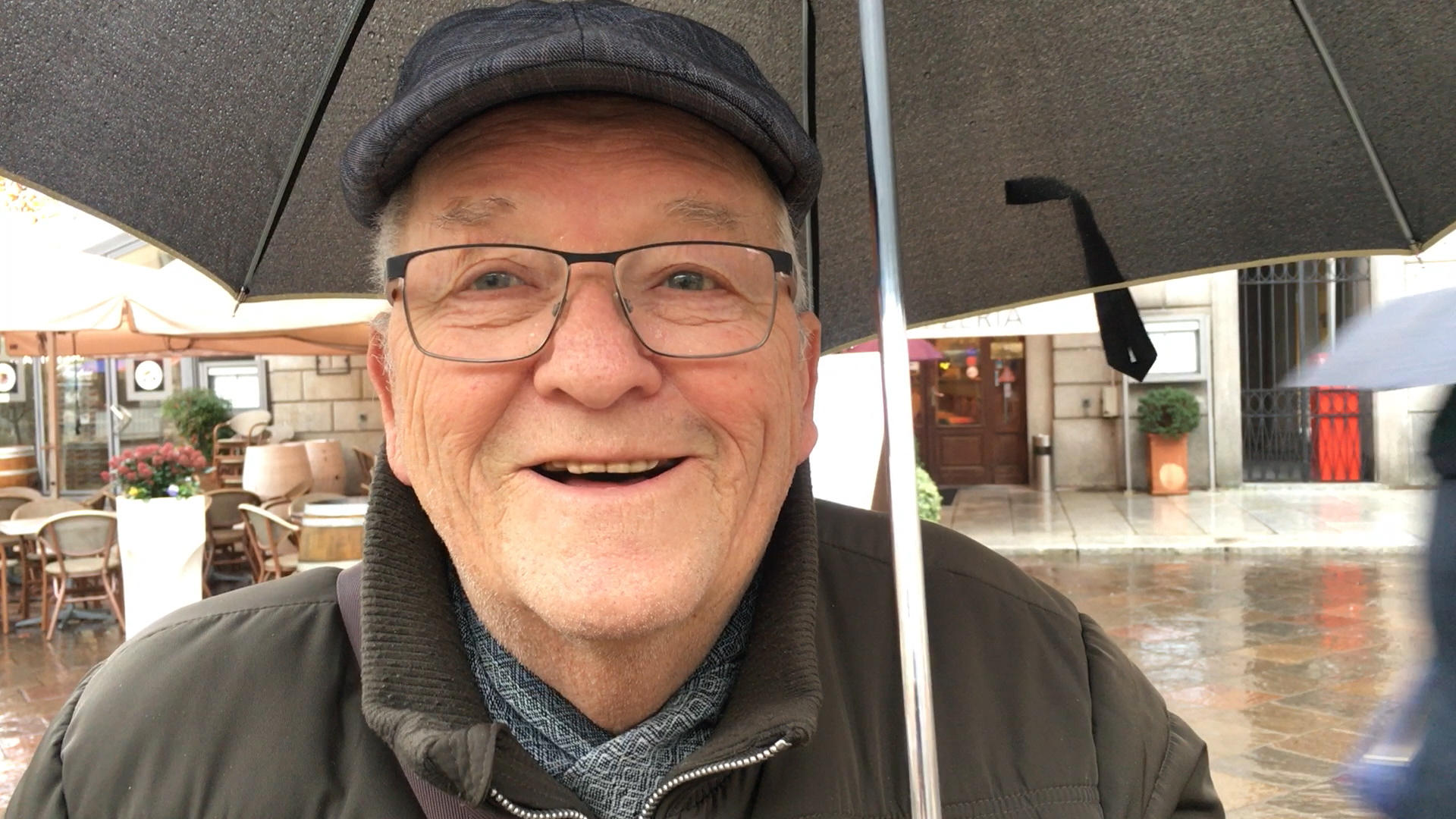 Mann mit Käppi unter einem Schirm