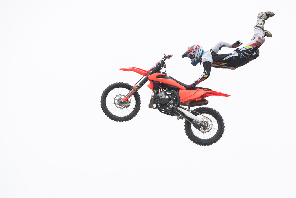 Motorbike rider hangs onto his bike with one hand as he flies through the air