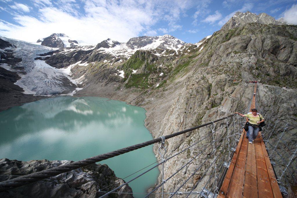 donna che cammina su una passerella sospesa sopra a un lago tra le montagne