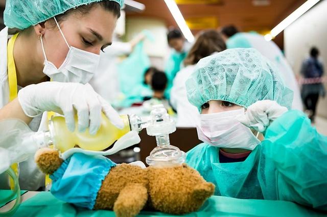 Una estudiante en Medicina y un niño atienden a un osito de peluche