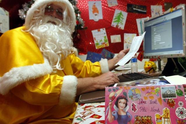 Un hombre vestido de Papá Noel lee una carta ante un ordenador.
