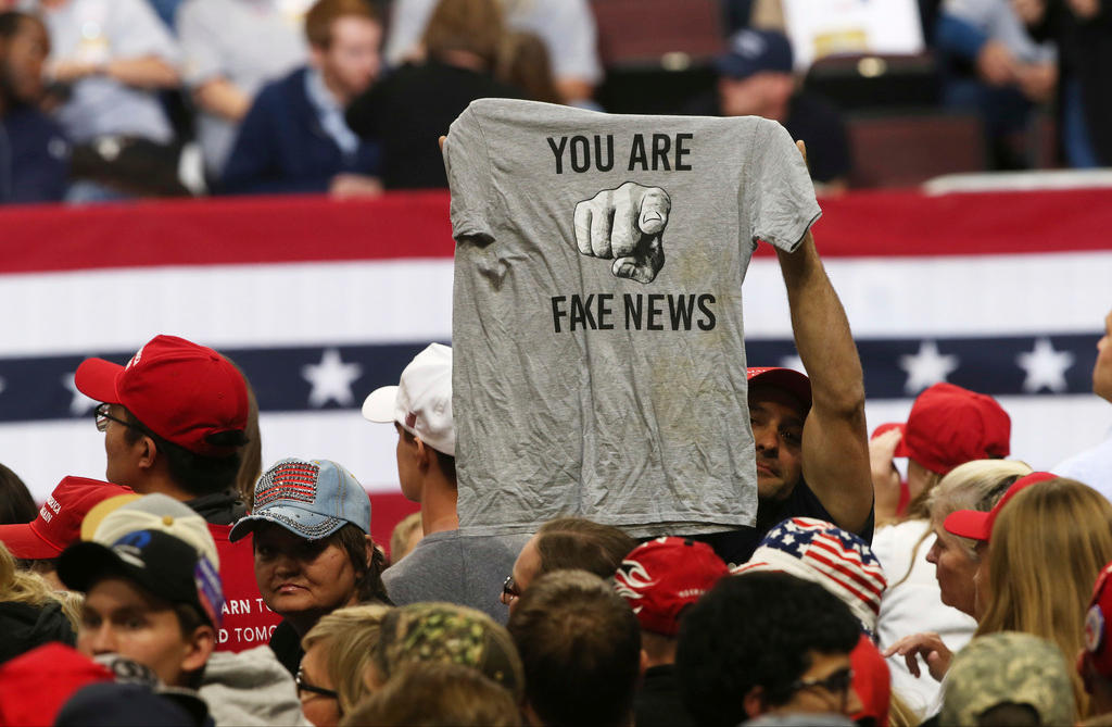 A crowd holds aloft a t-shirt with the logo You Are Fake News