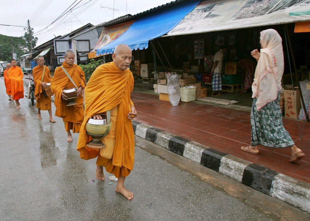 Buddhistische Mönche gehen auf einer Strasse, daneben eine Muslimin auf dem Bürgersteig.