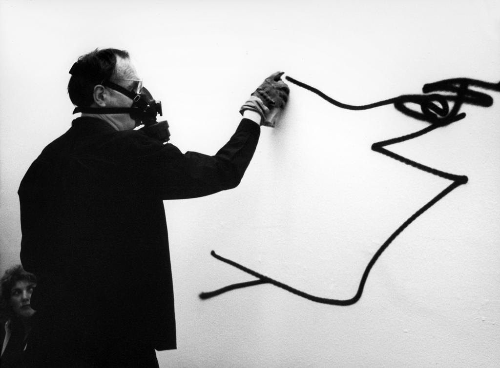 man spays a wall with ink while wearing a mask.