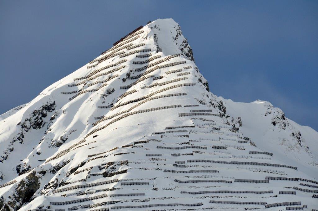 Cima di una montagna innevata dove ci sono barriere di protezione contro le valanghe.