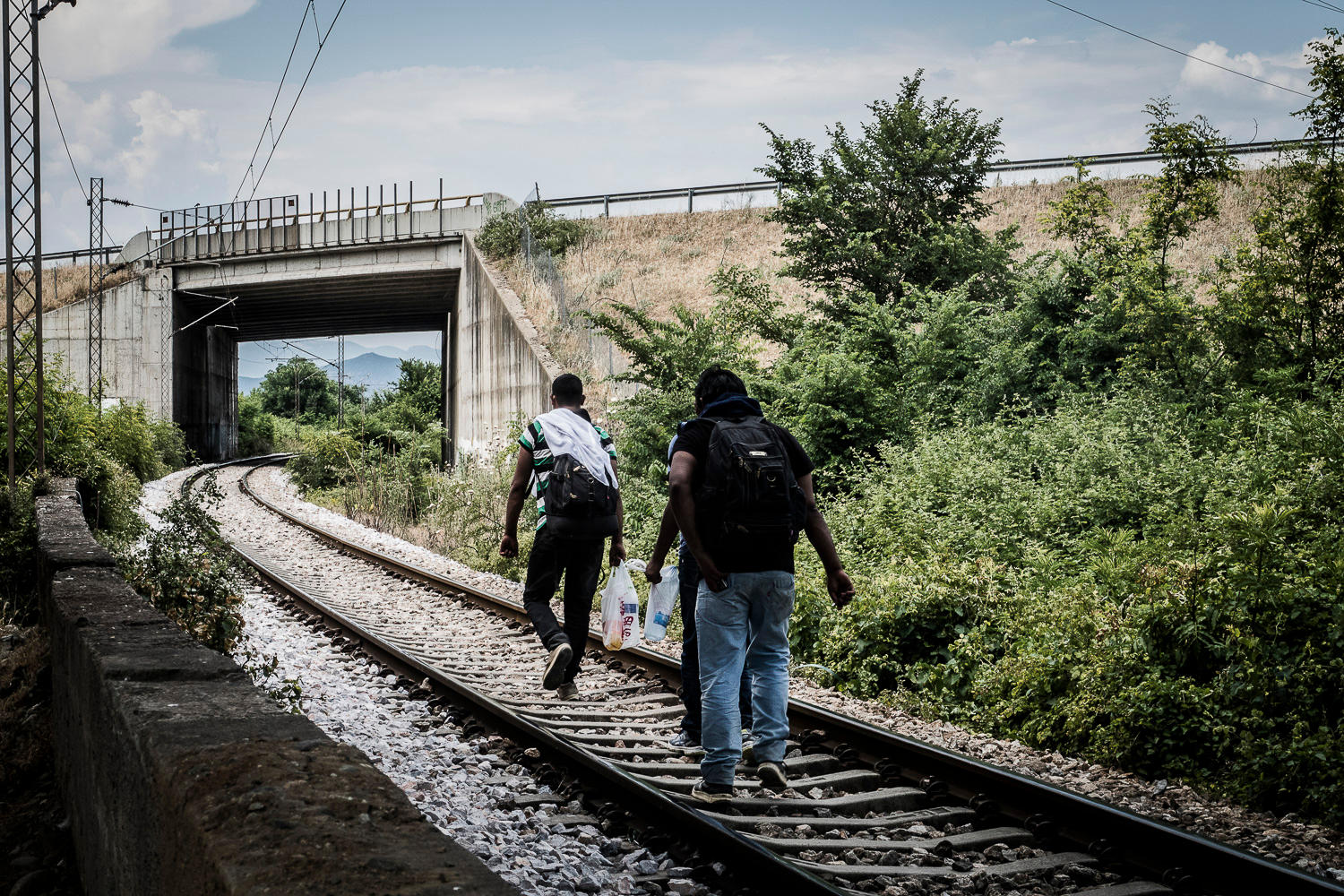 Three men walk on the tracks of a railway away from the camera.