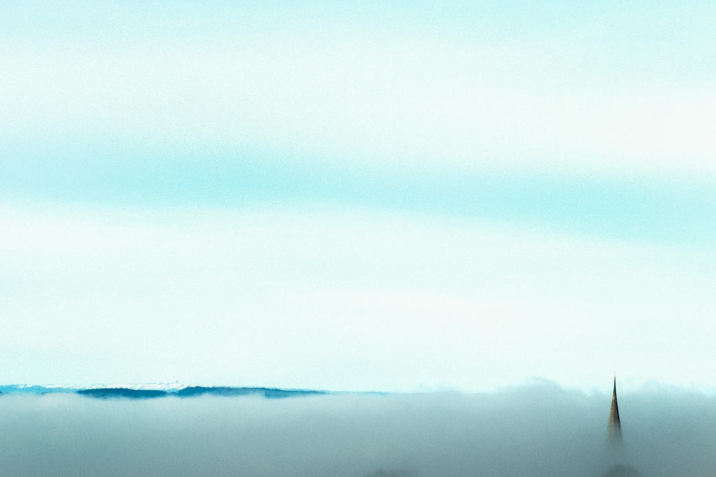 A church steeple sticks out of fog