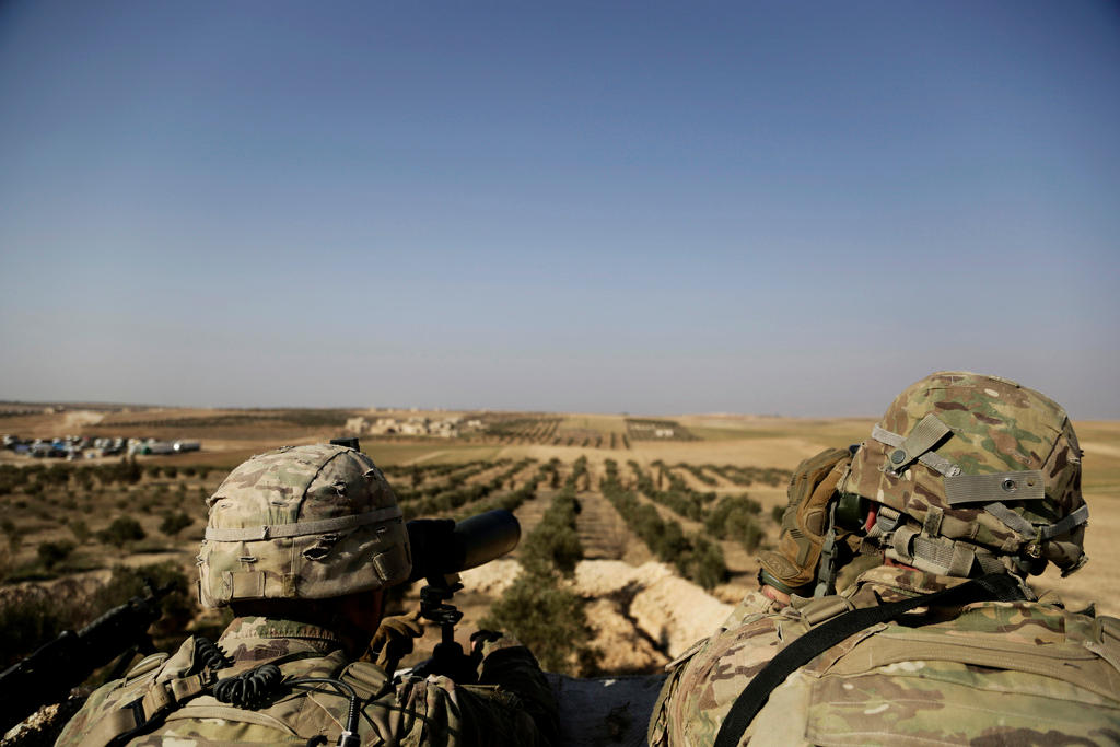Due militari con tuta mimetica e casco sdraiati, visti di schiena; davanti a loro paesaggio di campagna