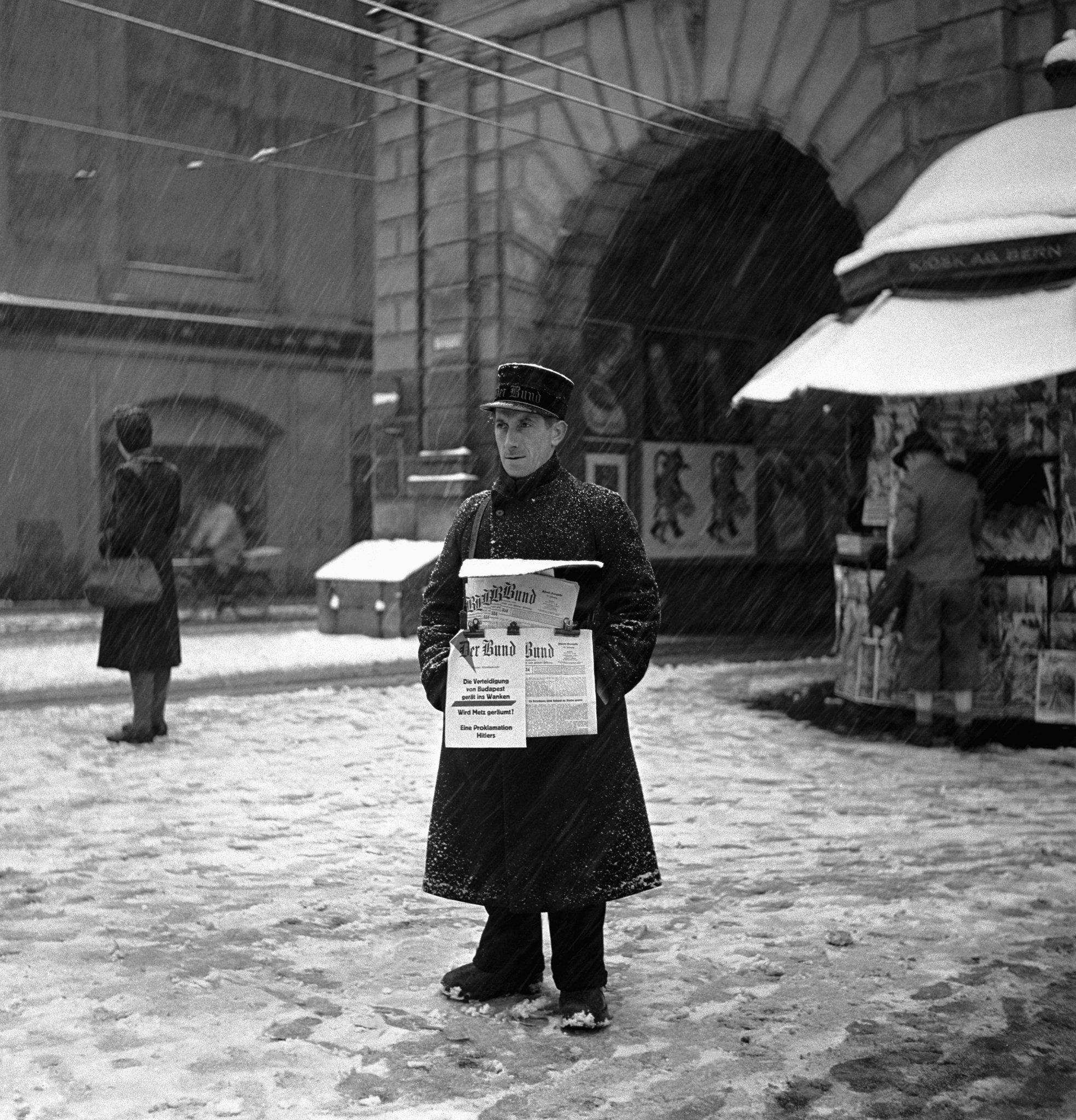 雪の中で新聞を売る男性