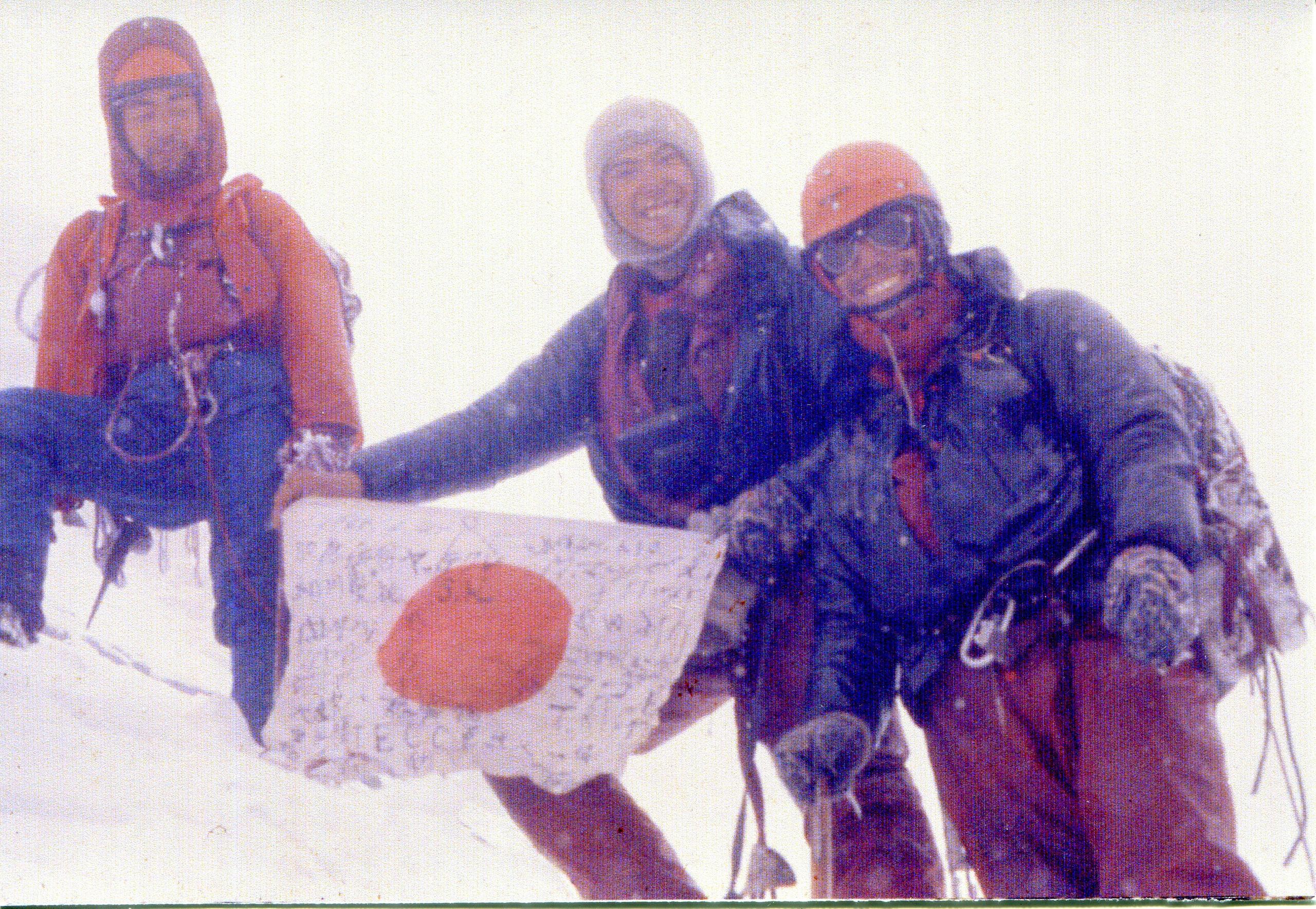 Three climbers on summit hold Japanese flag