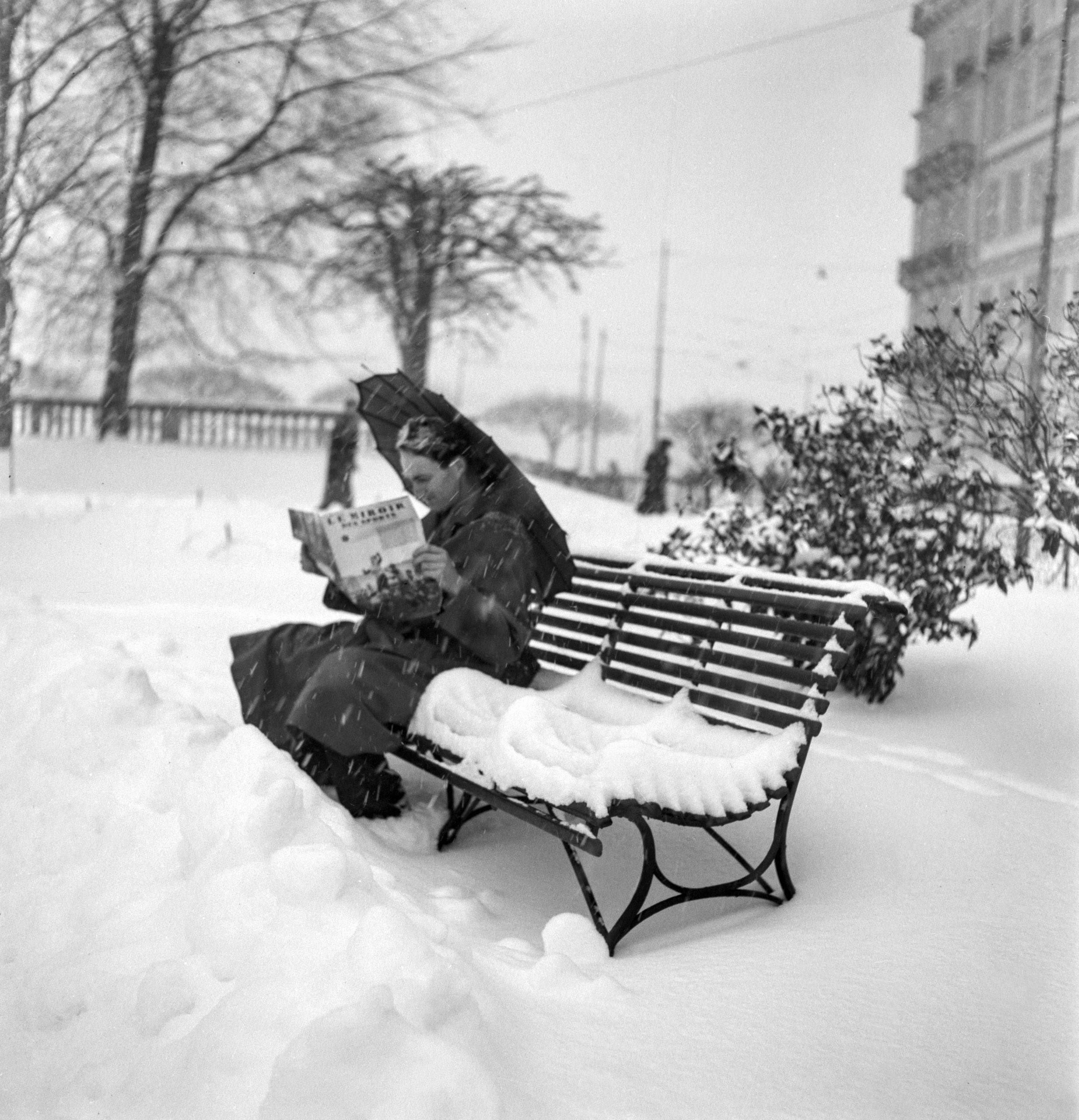 Una mujer lee un libro sentada en una banca nevada de un parque