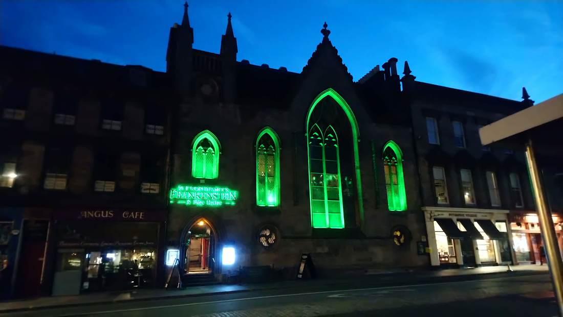 Immagine notturna di edificio che sembra una chiesa; si distinguono i contorni, gli archi gotici illuminati in verde, un insegna