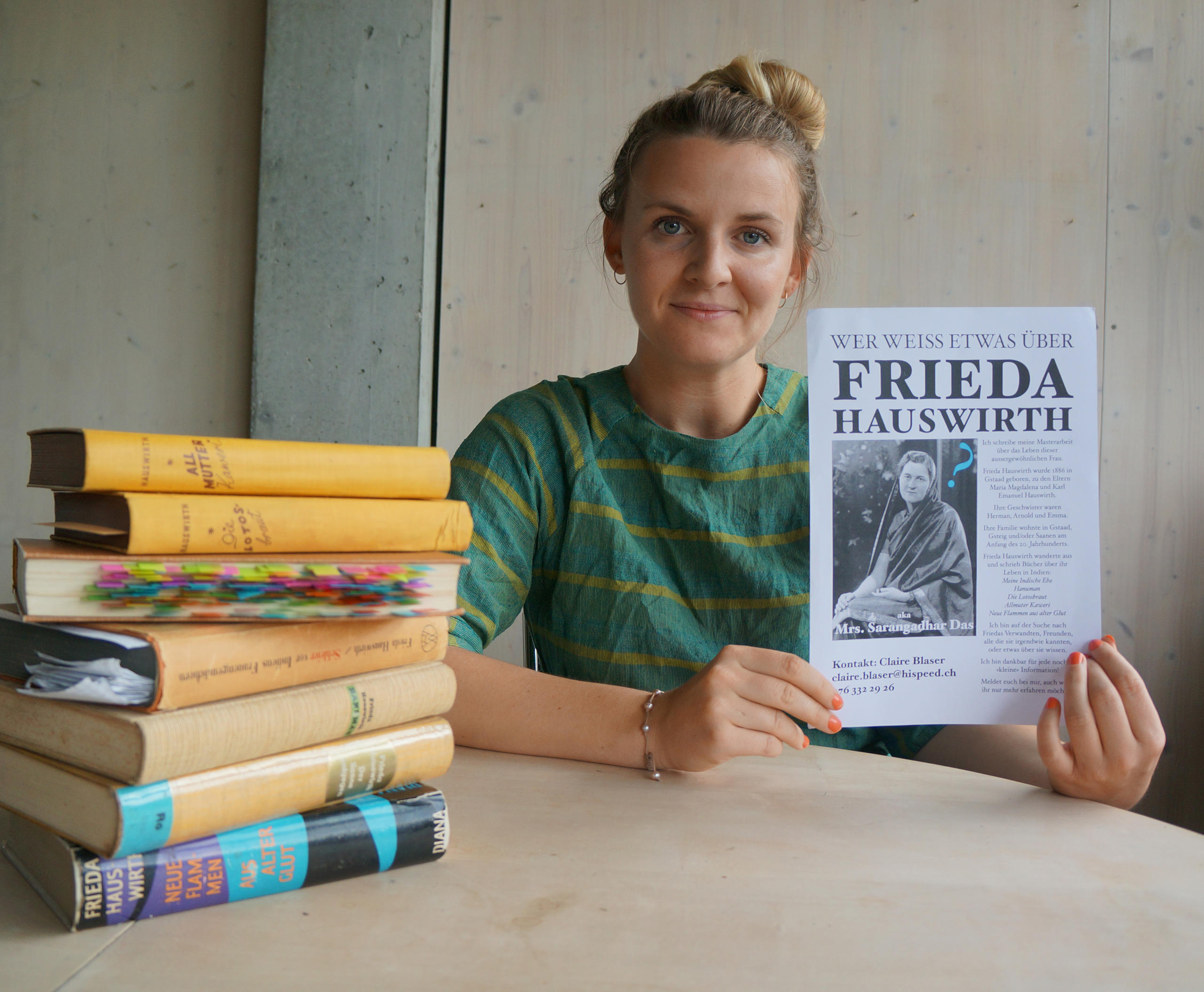 Eine Frau sitzt an einem Tisch mit Büchern und hält ein Blatt in den Händen.