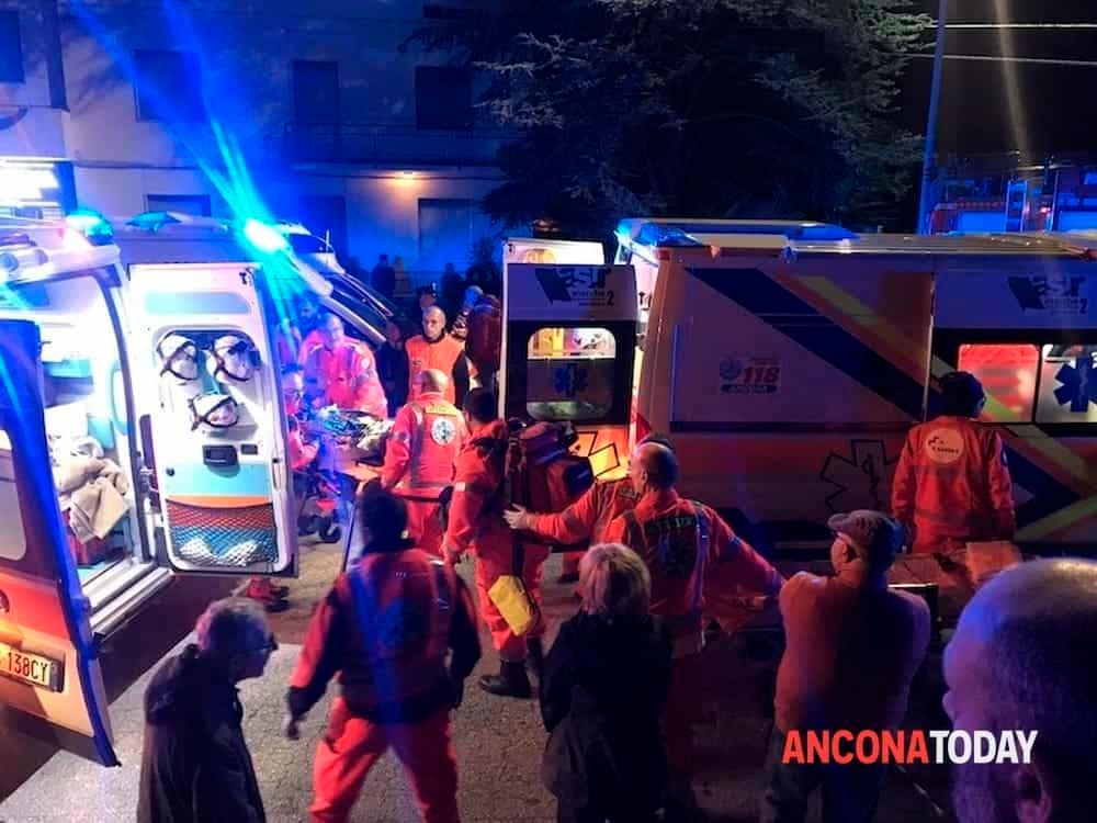 Esterno notte; due ambulanze con lampeggianti accesi e portellone posteriore aperto; soccorritori e altre persone attorno