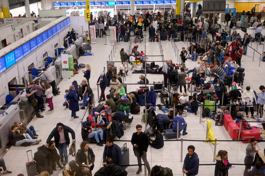 Area partenze di un aeroporto, con nastri divisori, e persone distribuite disuniformemente, in parte accampate