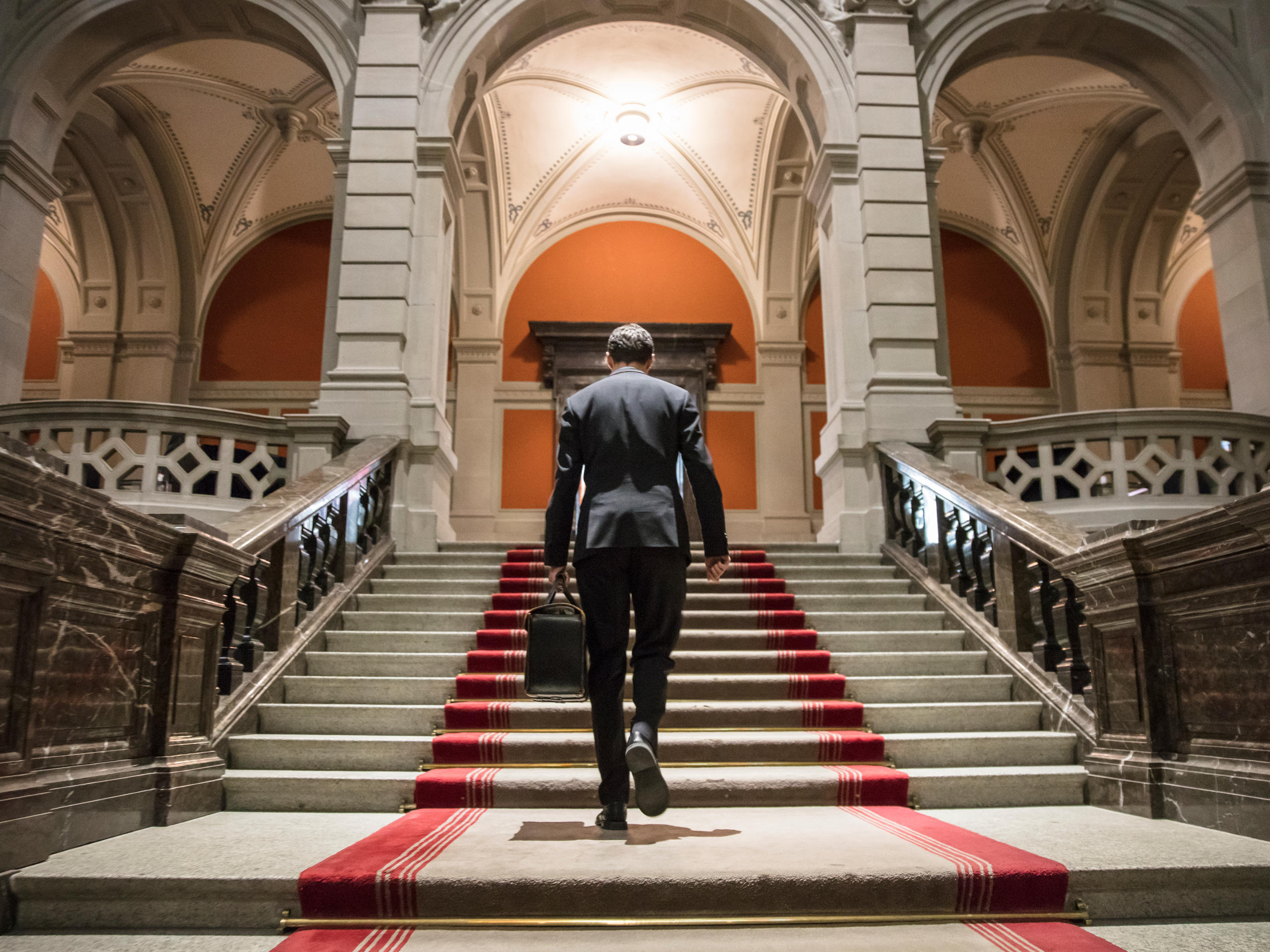 ein persönlicher Mitarbeiter, der eine schwere Aktentasche trägt, von hinten im Bundeshaus