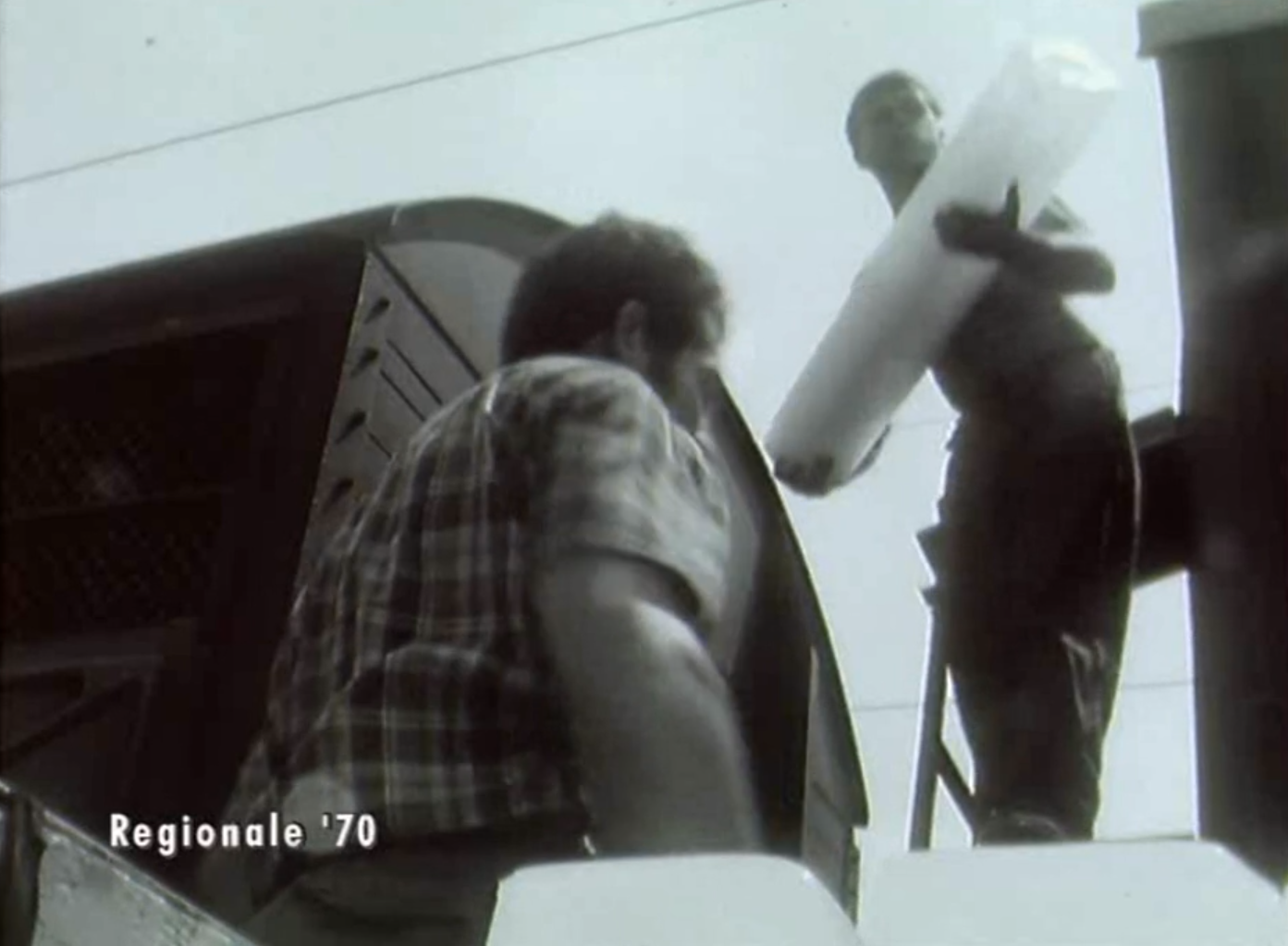 Un uomo in piedi tra due vagoni ferroviari solleva una barra di ghiaccio; un altro si appresta a passargli la successiva