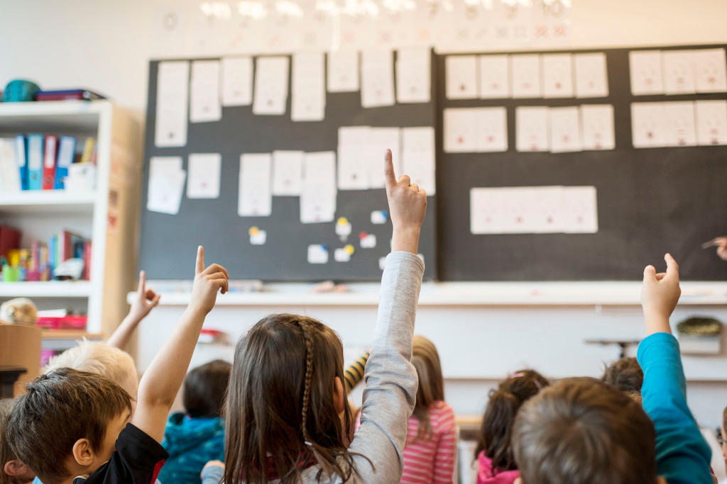 children raising hands in classroom