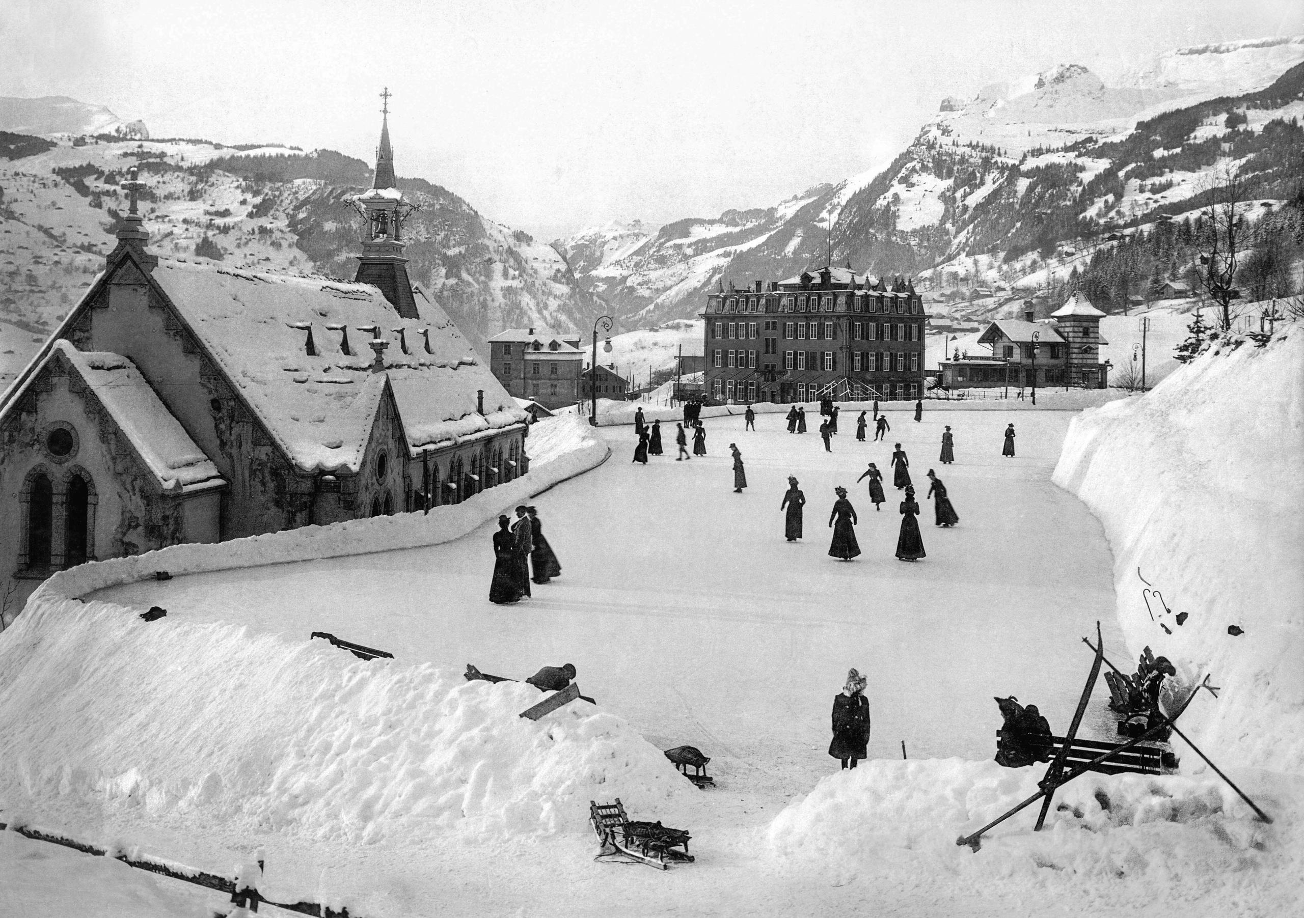Paisaje invernal de montaña. En el centro, unas personas patinan en una pista de hielo al lado de una iglesia
