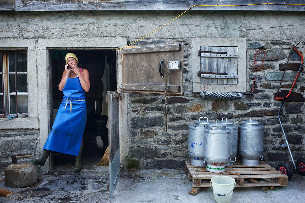 A woman stands smoking in the doorway to a farmhouse