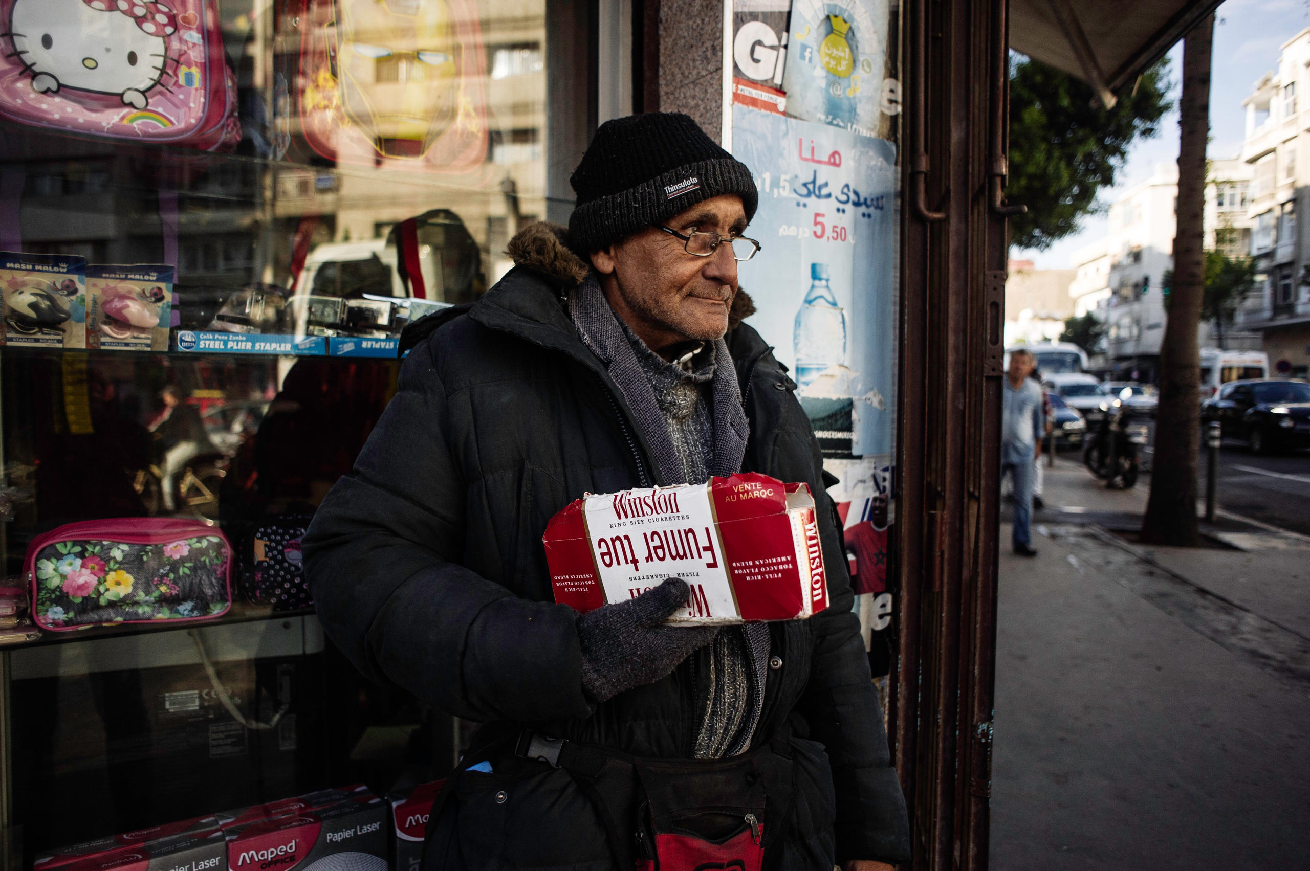 Un hombre mayor sale de una tienda con un cartón de cigarrillos en la mano