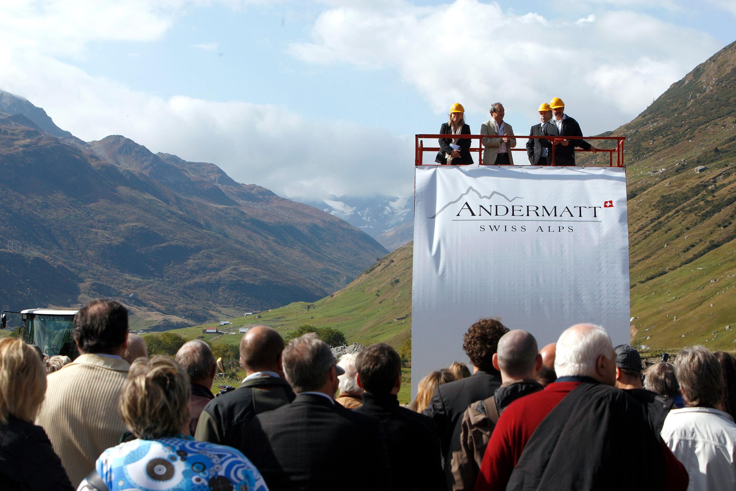 Spatenstich in einem Hochtel. Auf einem Podest vor einer Menschenmenge vier Personen. Schriftzug Andermatt Swiss Alps