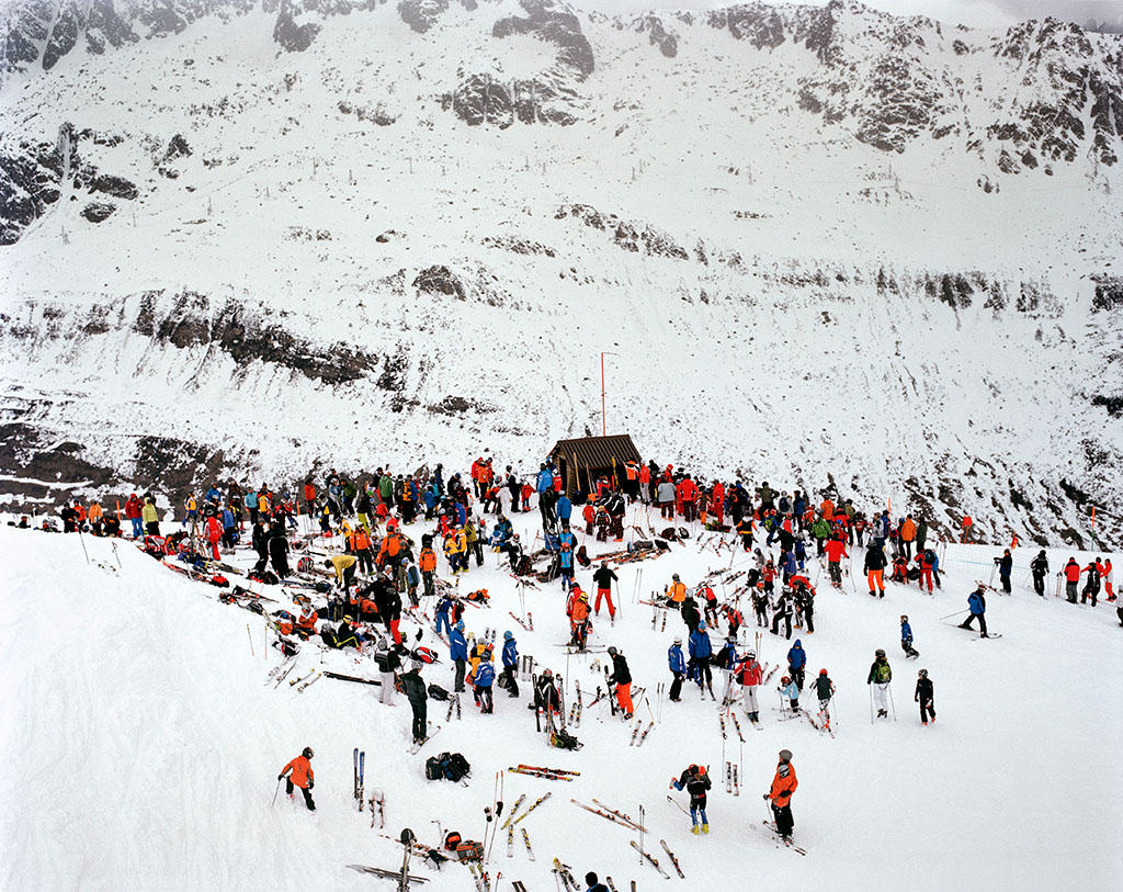 Assembramento di persone in tuta da sci e con gli sci sul cucuzzolo di una montagna innevata