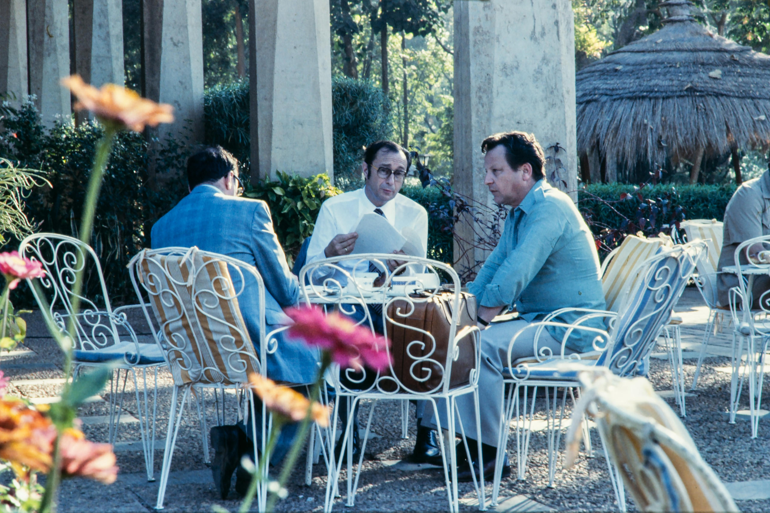 ثلاثة رجال يتبادلون أطراف الحديث حول طاولة في الهواء الطلق