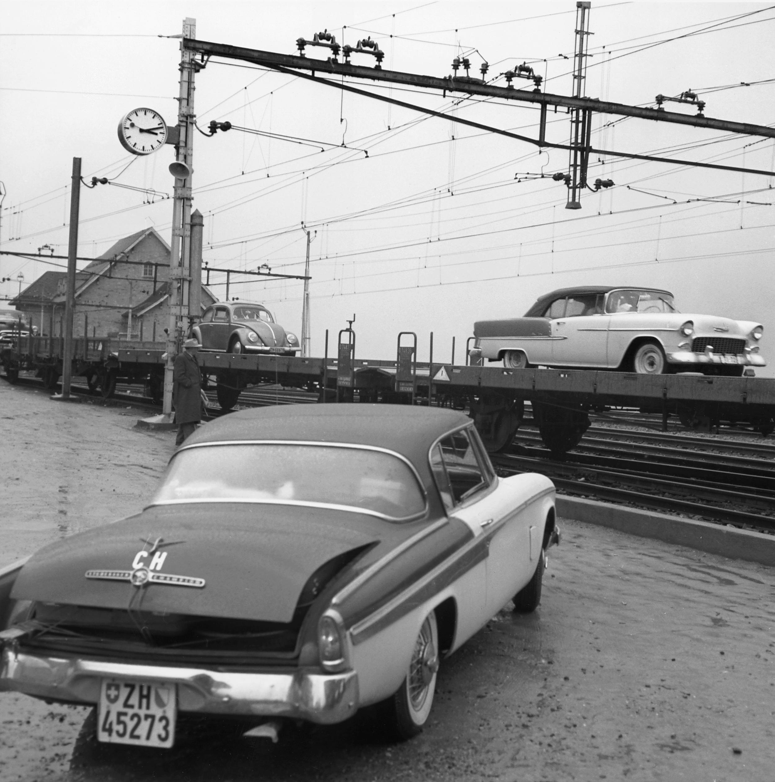 Auto im 1950er-Design beim Autoverlad auf die Bahn. Bahnhofsuhr im Hintergrund