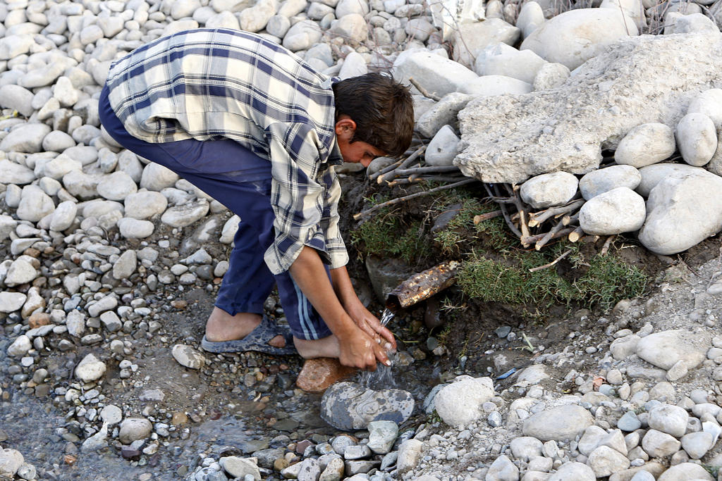 A boy washes his hands at a broken water pipe