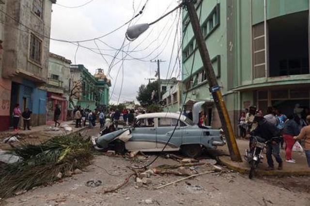 Una calle en La Habana con un poste a medio caer y un coche aplastado