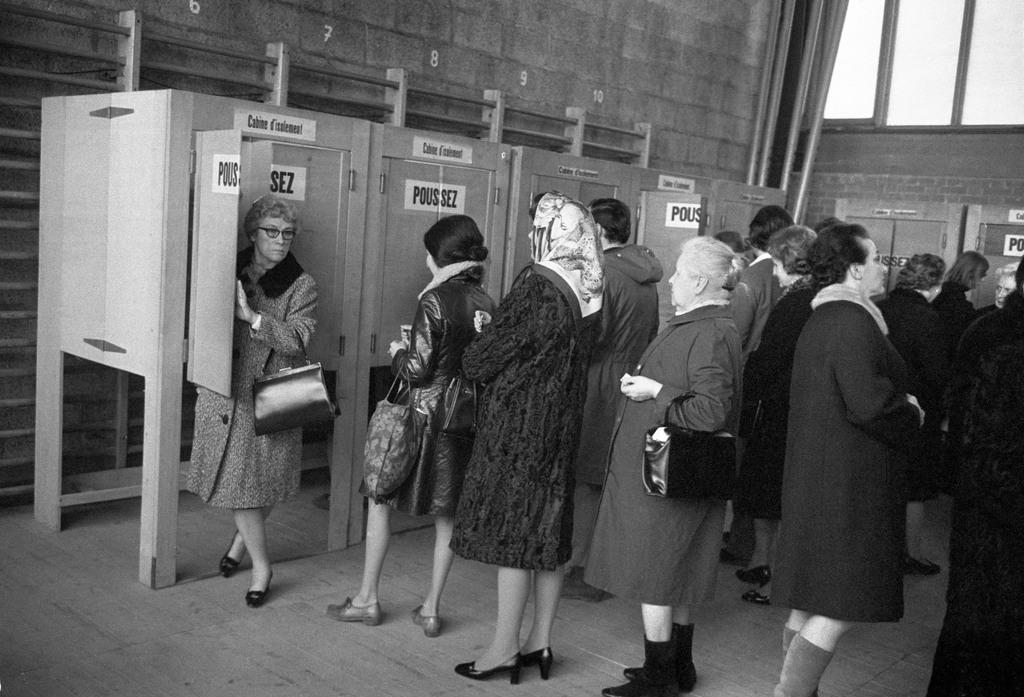 Immagine in bianco e nero di donne in coda davanti a cabine elettorali con scritte in francese