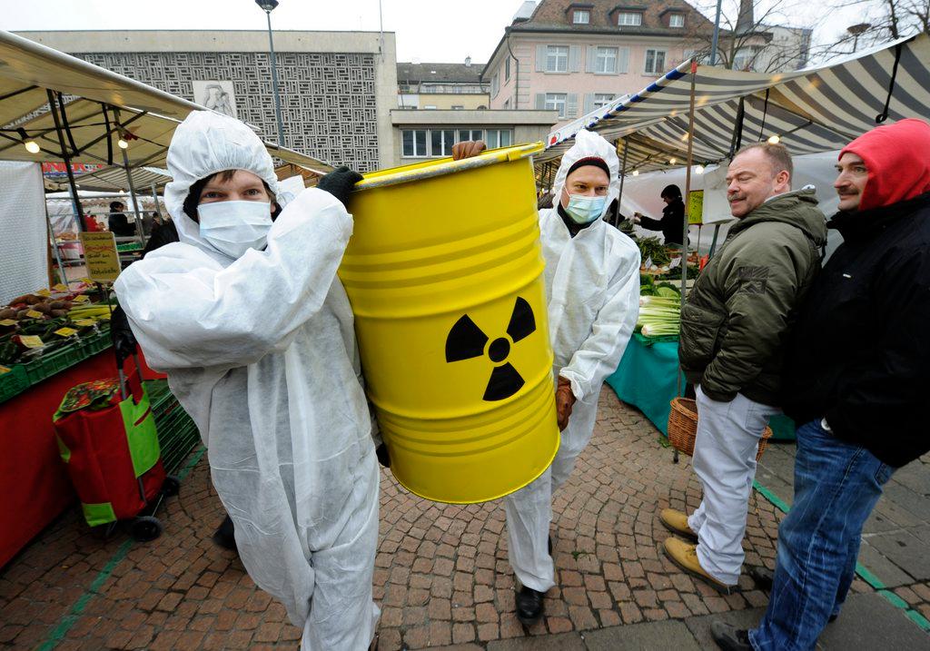 Zwei Personen in weissen Overalls tragen ein gelbes Fass mit dem Symbol der Radioaktivität