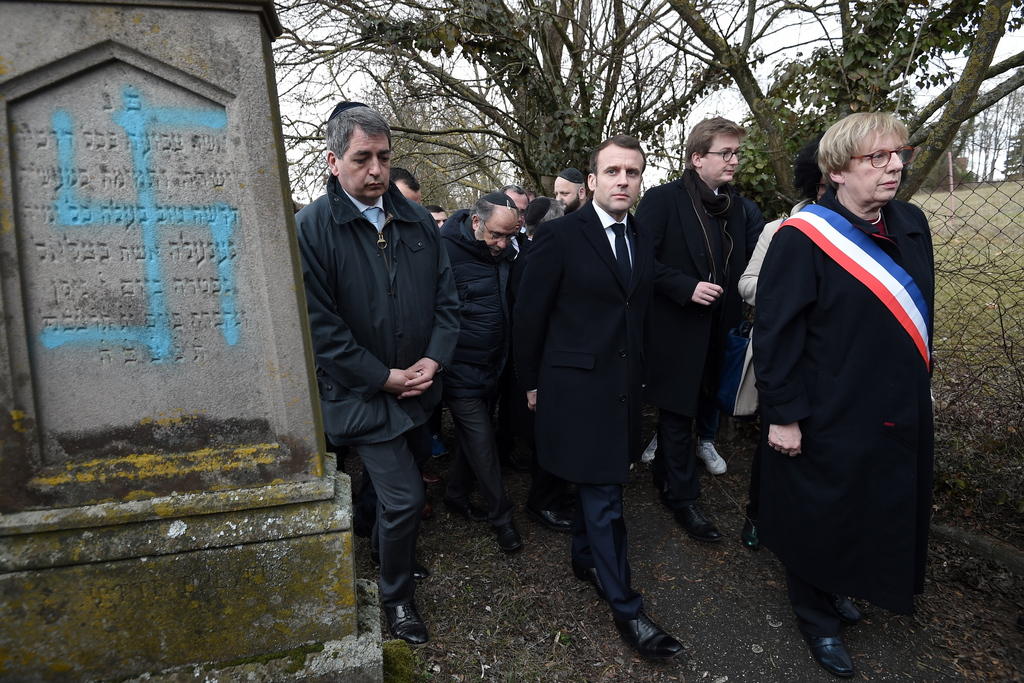 macron accompagnato da diverse persone accanto a una tomba profanata