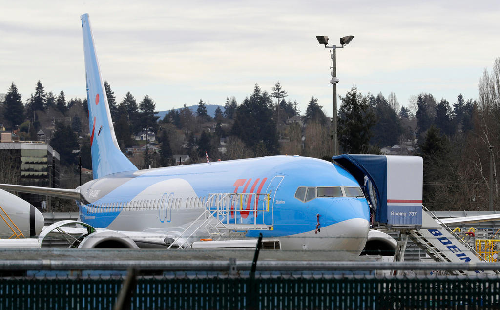 Immagine di un aereo con logo TUI scattata da dietro una rete metallica; si vede scaletta con scritta Boeing