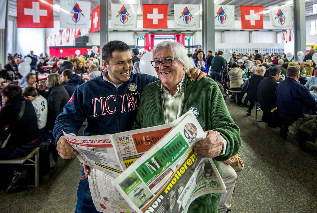 Zwei Männer halten zusammen eine Zeitung in der Hand und lachen.
