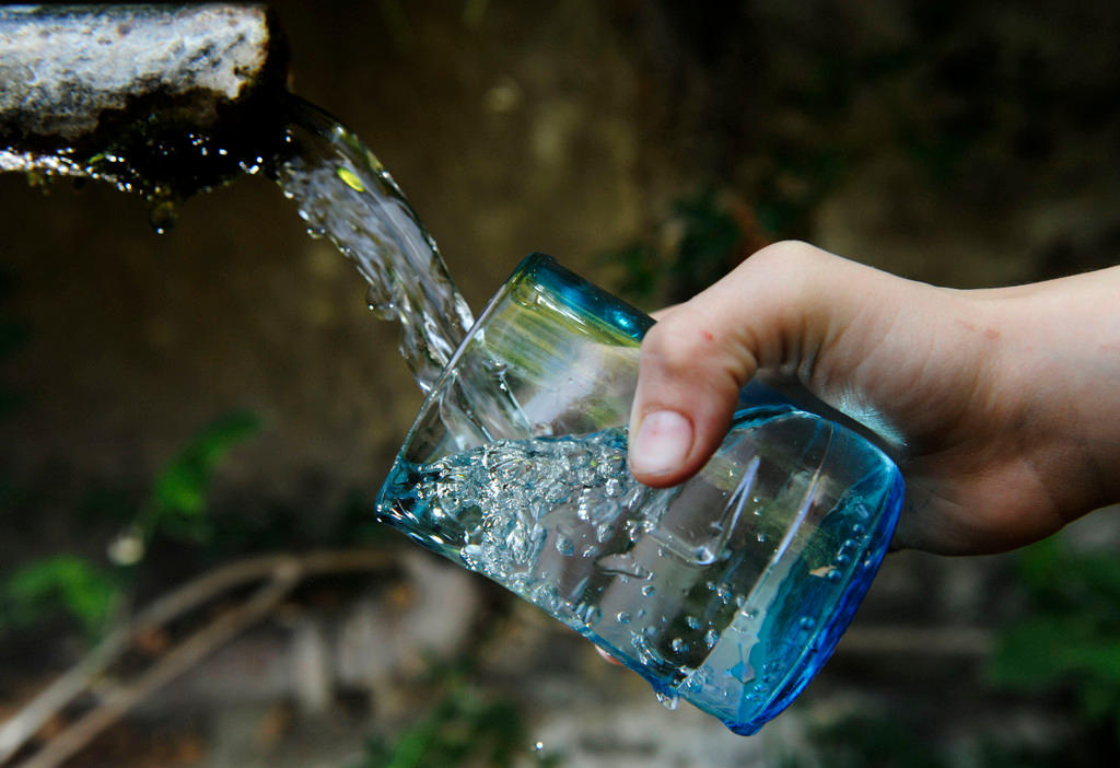 mano che riempie un bicchiere con l acqua di una fontana